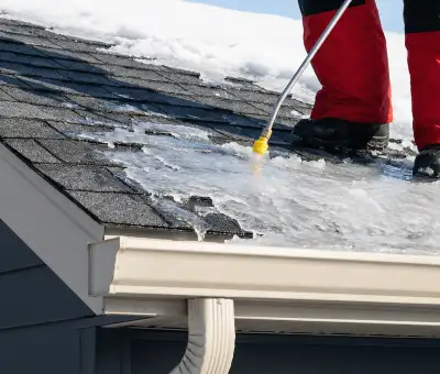 Ice dam removal technician using a steam wand to melt thick ice buildup on a residential roof in Toledo, OH