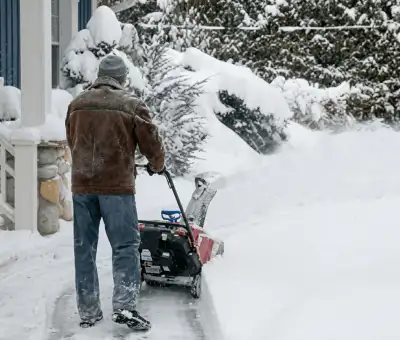 Residential snow removal technician using a snow blower to clear a home driveway and walkway in Toledo, OH