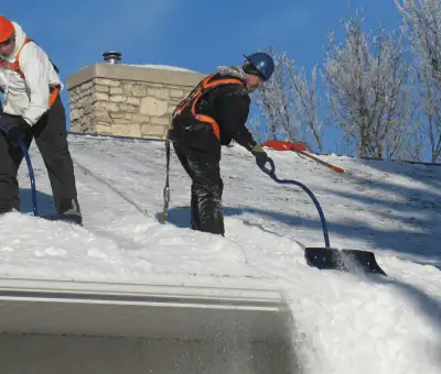 Professional technicians performing roof snow removal with safety harnesses and shovels in Toledo, OH